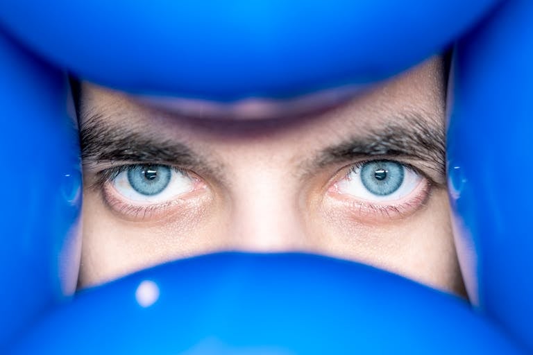 Close-up portrait of a person with striking blue eyes surrounded by vibrant blue balloons.
