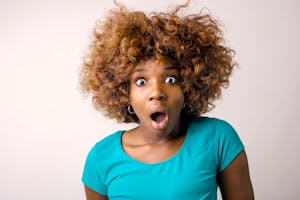 Portrait of a surprised woman with curly hair in a teal top on a white background.