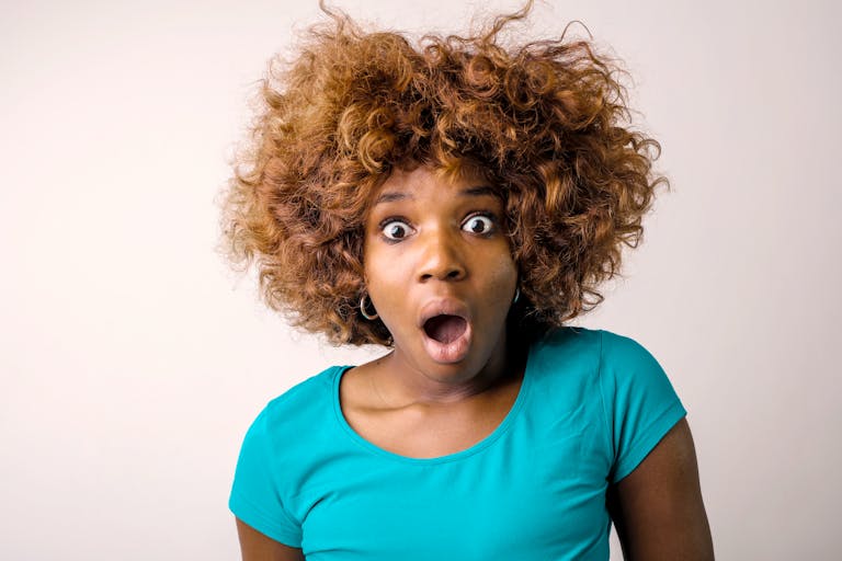 Portrait of a surprised woman with curly hair in a teal top on a white background.