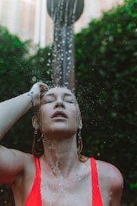 A woman enjoying a refreshing outdoor shower, wearing a red tank top.