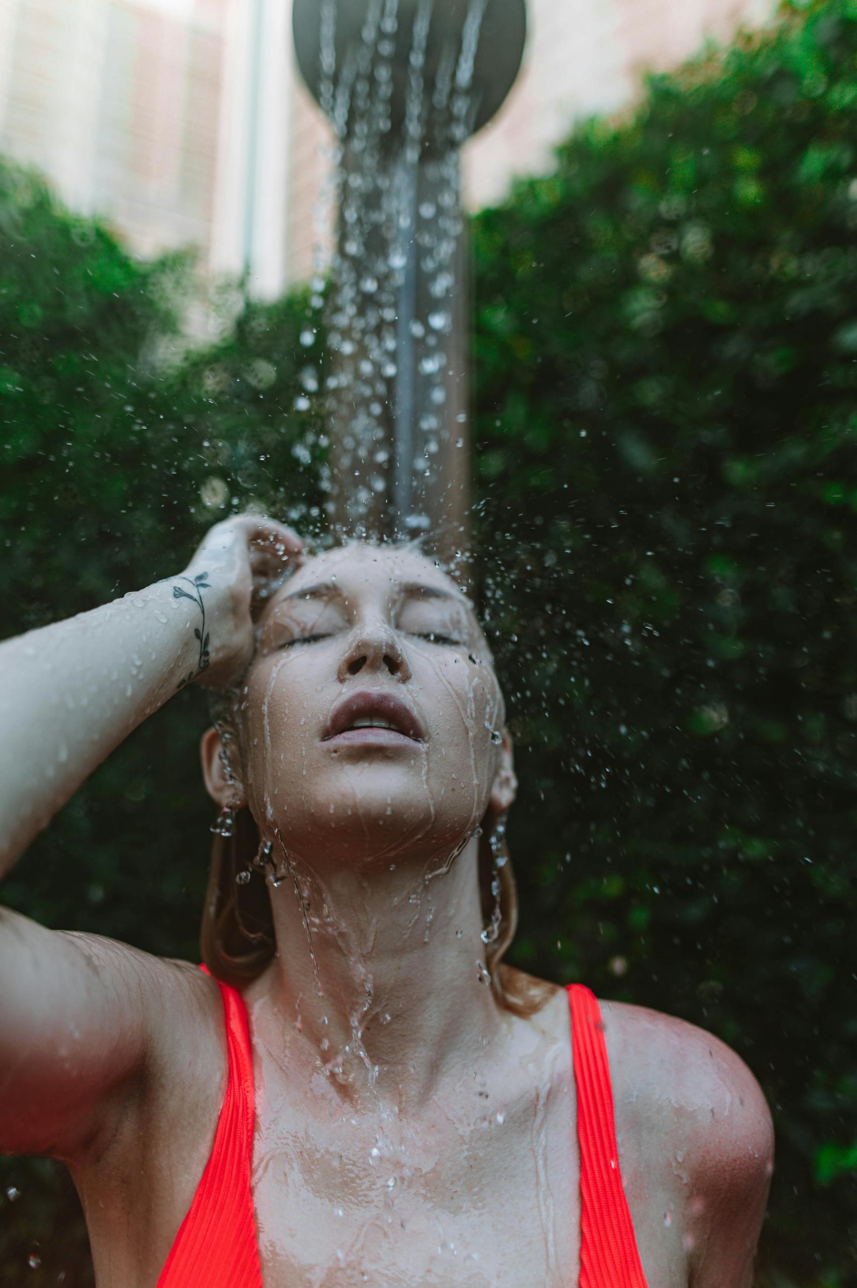 A woman enjoying a refreshing outdoor shower, wearing a red tank top.